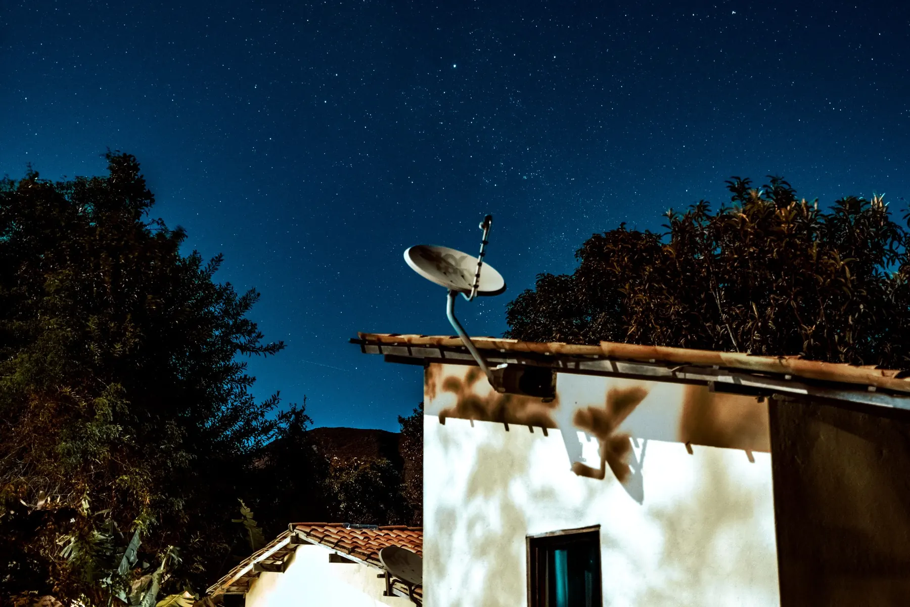 Satellite dish on a small house under a starry night sky